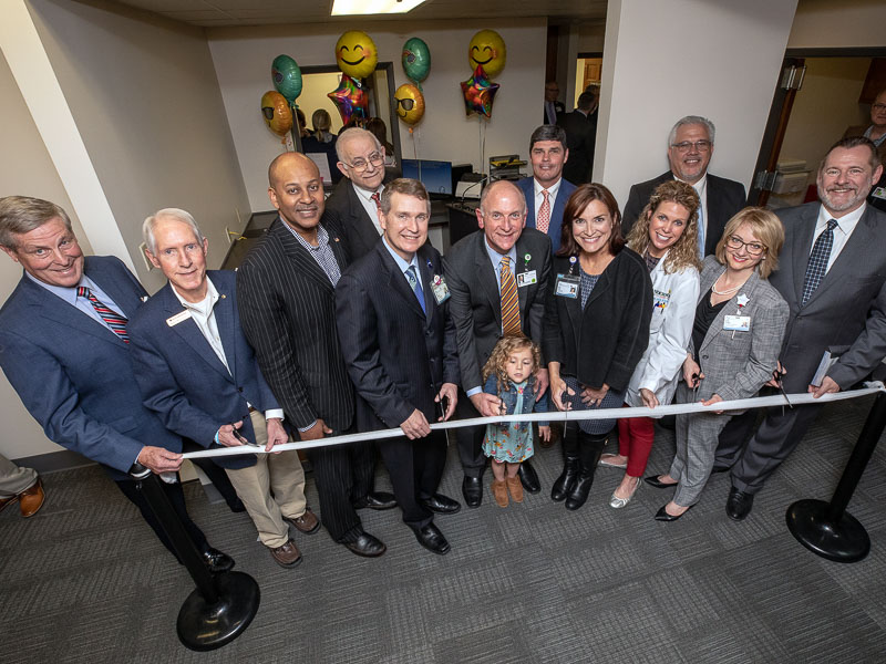 Group of people smiling before a ribbon cutting.