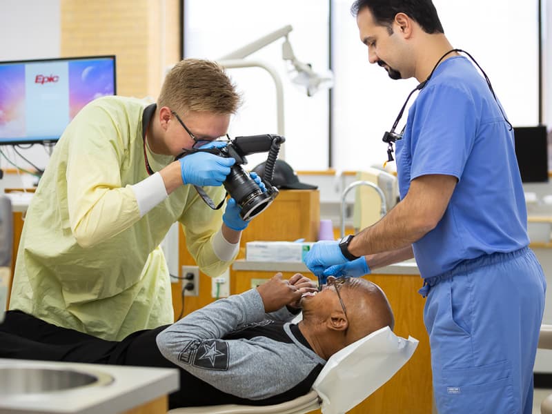 Taylor Bolland, third-year dental student, photographs patient Mike Evans' mouth while Dr. Firas Mourad, professor of dentistry, holds an instrument to keep Evans' mouth open.