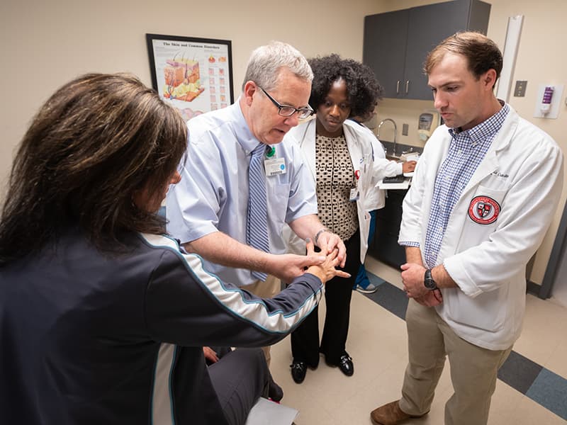 Brodell with patient describing a dermatological condition to two M4 students