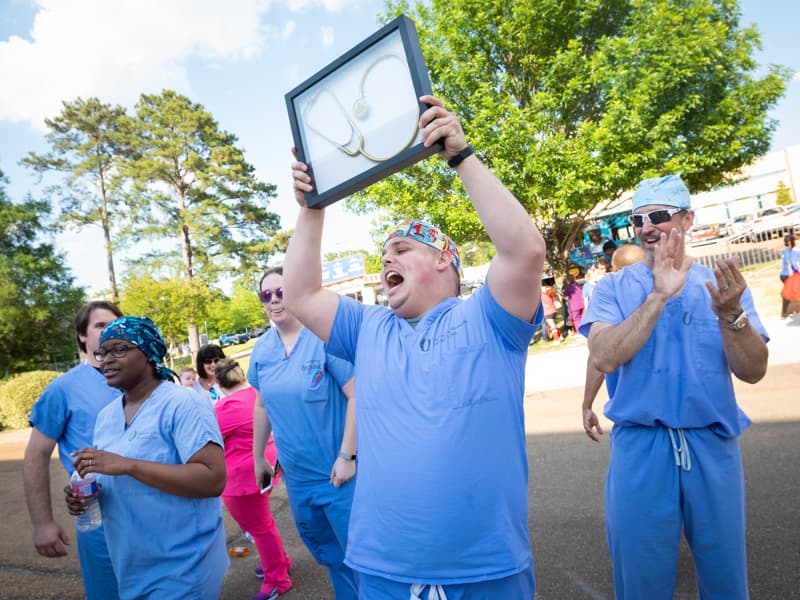 Batson OR registered nurse Kyle Dickerson hoists the Golden Stethoscope awarded to the winning team in the 2018 gurney races.