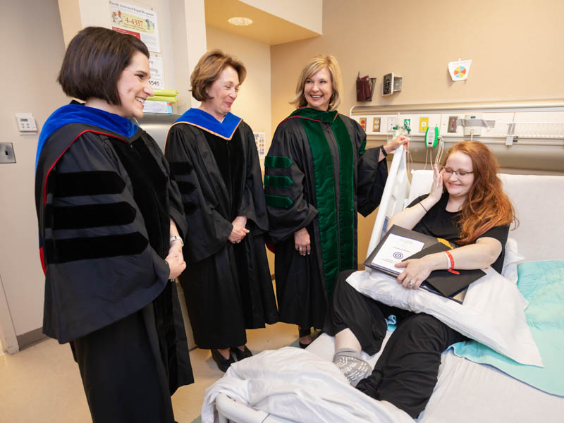 Sarah Herrington is overwhelmed by the kindness of those who brought graduation to her hospital room, including Dr. Kristi Moore, left, Dr. Jessica Bailey, second from left, and Dr. LouAnn Woodward.