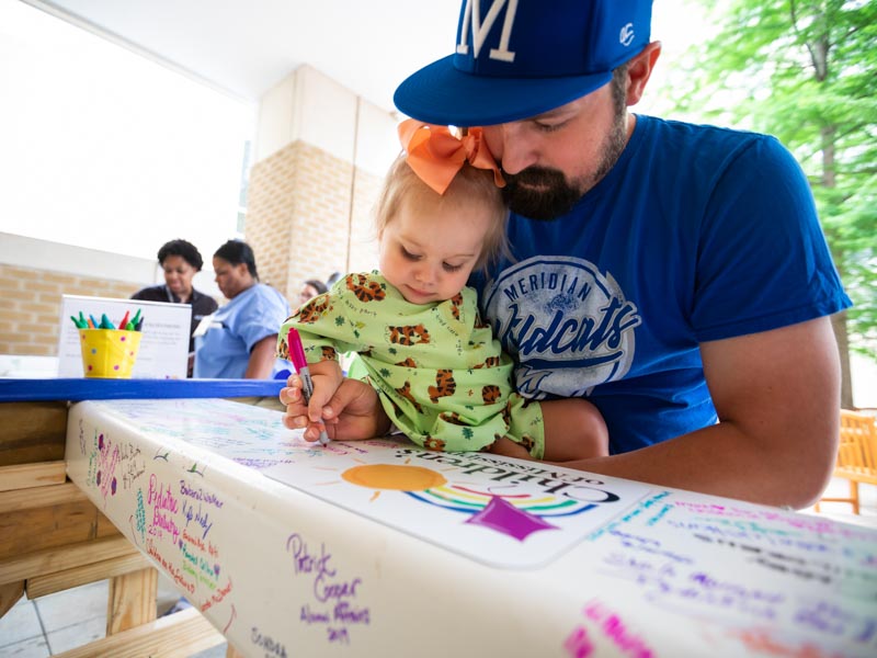 Jacob Drury of Philadelphia helps daughter Kinsley, a Batson patient, sign the beam.