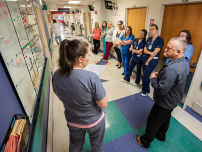 Registered nurse Anna Odom, left, leads a morning huddle on 2 Children's as nurse manager Wesley Smith, right, and other floor staff look on.