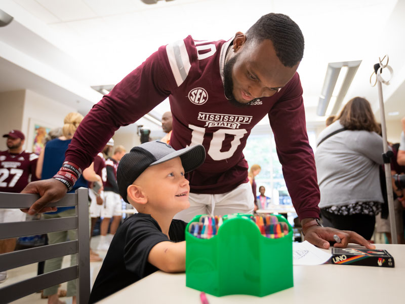 Mississippi State linebacker Leo Lewis watches as patient Lane Smith of Waynesboro colors during an afternoon play session at the state's only children's hospital.