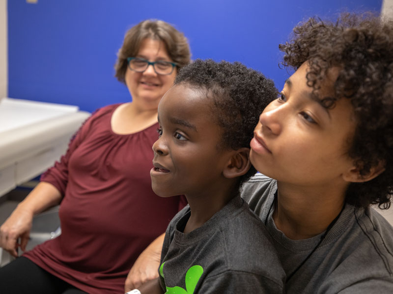 Elizabeth Barber of Bassfield looks on as son Jarvis, held by her daughter, Anna, gets a genetic consultation through telehealth.