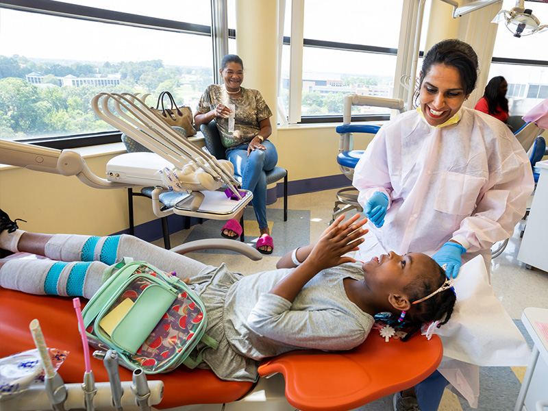 Marsha Jones laughs as her chair lifts her back up to a sitting position, one of her favorite parts of going to the dentist, while her grandmother, Eva Harper, left, and Dr. Susmitha Koti, chief pediatric dentistry resident, watch.
