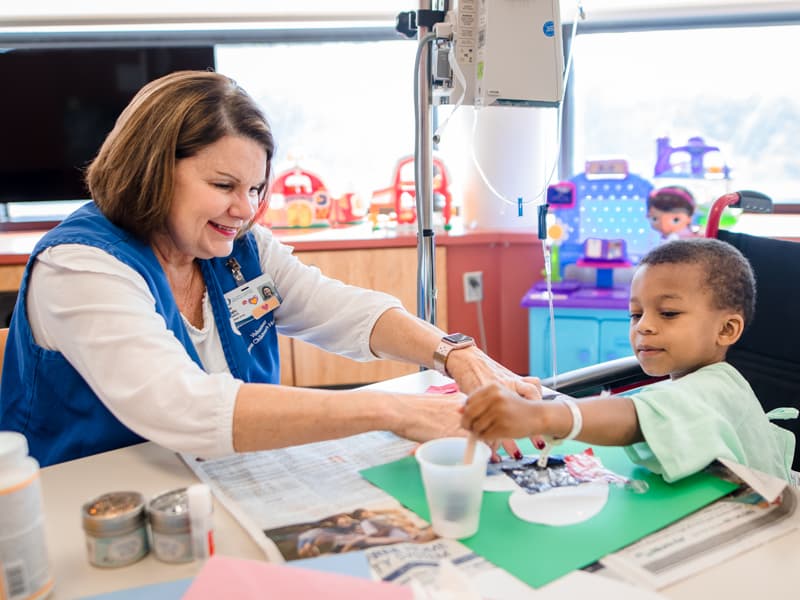 Begley helps Children's of Mississippi patient Joby Duck Jr. of Edwards glue tissue paper to his art project.