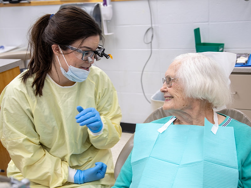 Female dental student talks to elderly patient.