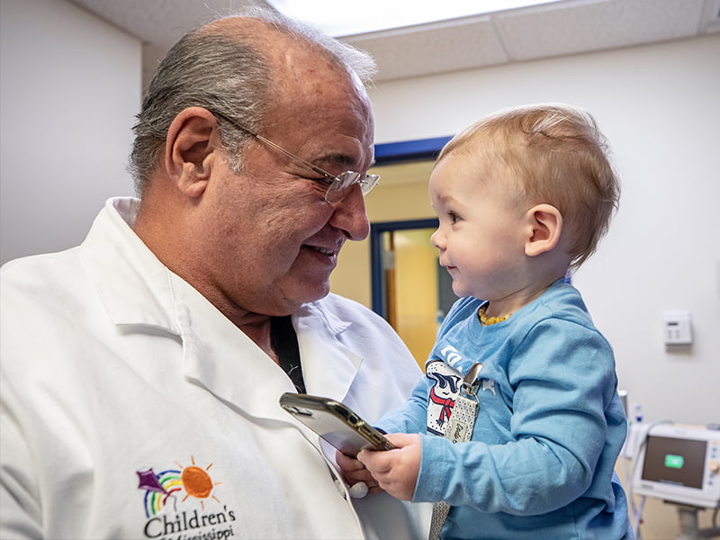 Dr. Barraza in a white coat holds a pediatric patient as they look at each other.