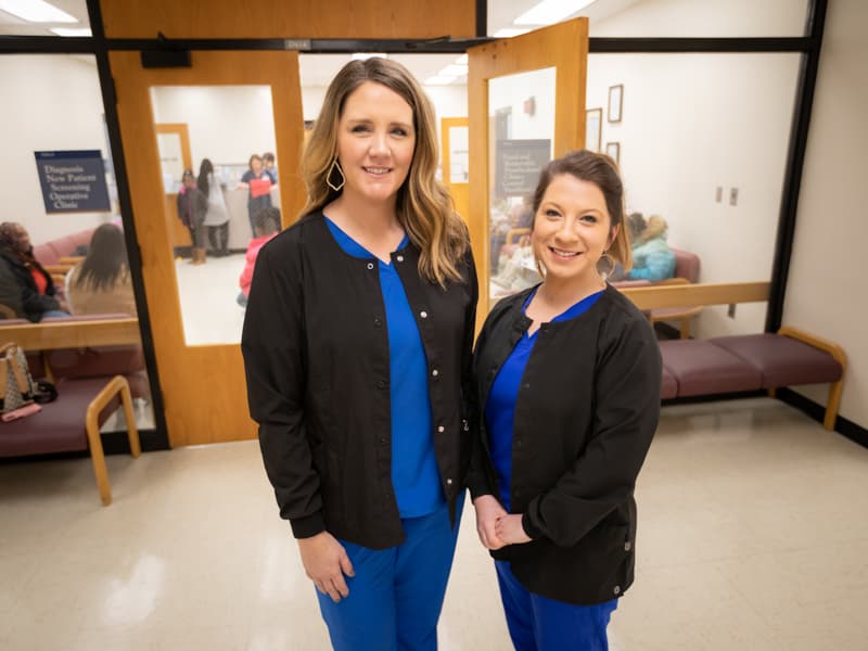 Two women pose for portrait in front of dental clinic doors.