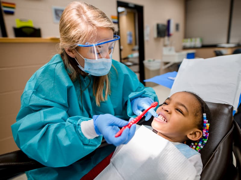 Dental student brushes girl's teeth.