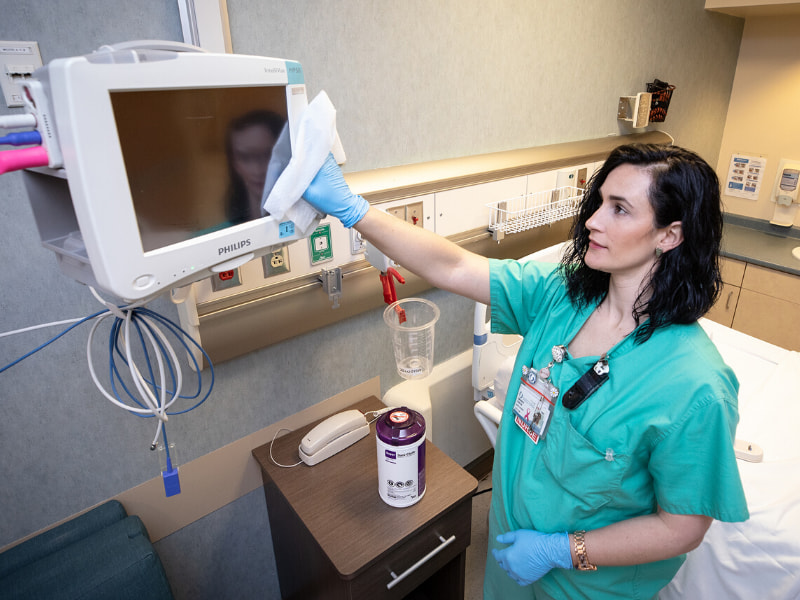 Nurse wears gloves and uses a disinfectant wipe to clean equipment.