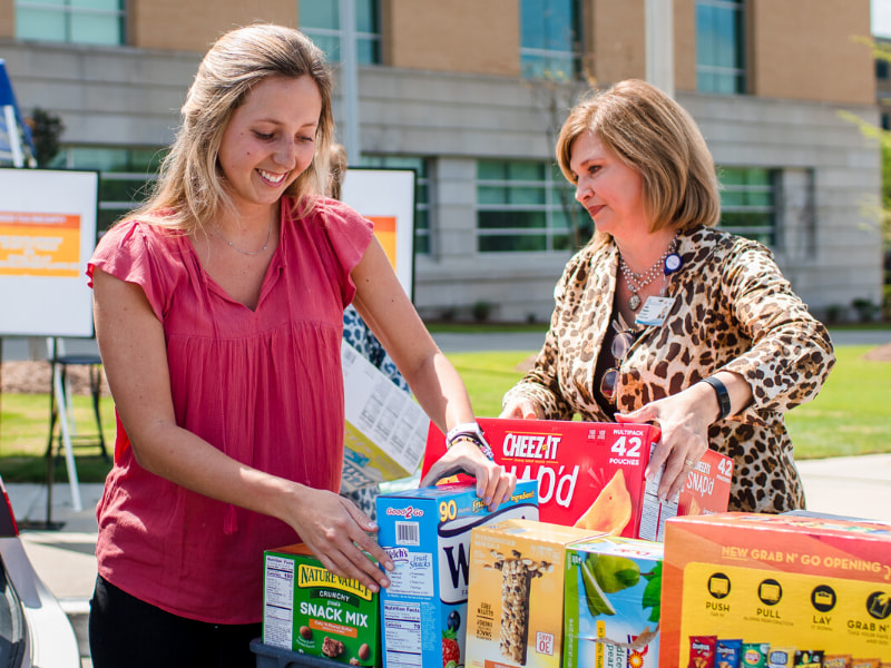 Olivia Woodward, left, and her mom, Dr. LouAnn Woodward, vice chancellor for health affairs and dean of the School of Medicine, hand off donations for COVID-19 relief at the Medical Center at a dropoff station in front of the School of Medicine.