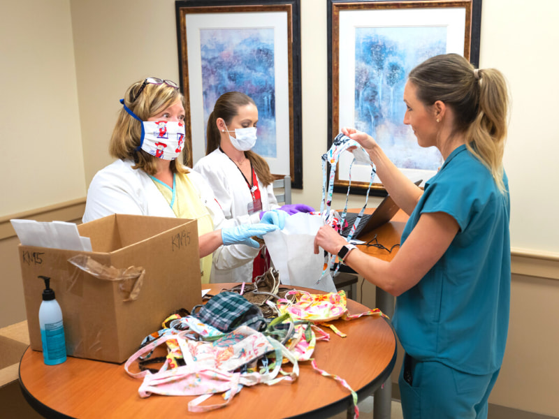 Registered Nurse Heidi Johnson, left, gives a mask to Registered Dietitian Lauren Page, right.