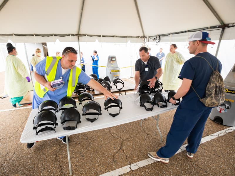 Left to right, Thomas Douglas, RN, Thomas Moak, polysomnographic tech, and Aaron Arnold, polysomnographic tech, sanitize face shields at the fairgrounds testing site.