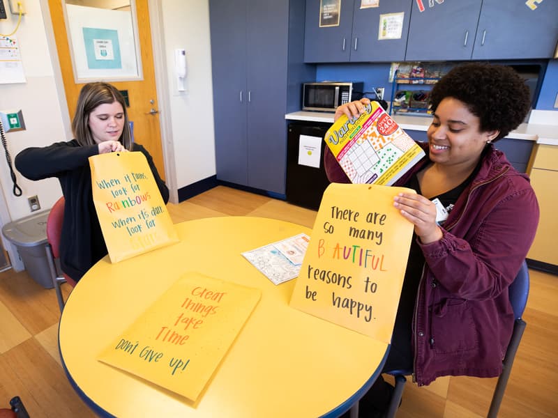 Morgan Flournoy, left, child life specialist, and Erinn Funches, child life assistant, prepare COVID-19 resourse packets for pediatric patients and their families. (Photo taken before implementation of CDC guidelines calling for all individuals to wear masks.)