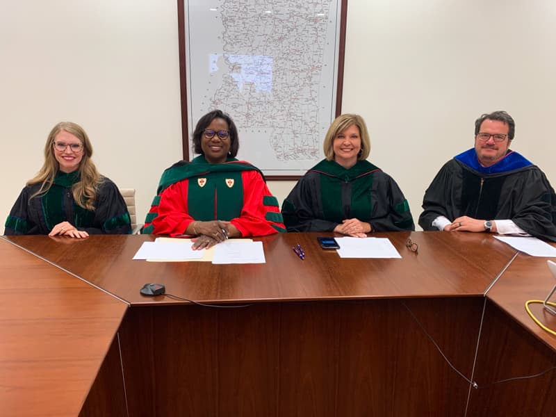 Four leaders officiating during the online Class of 2020 Commencement behind desk.