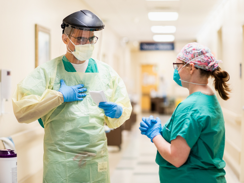 Heidi Logan, nurse on 2 North, assists Dr. Hamid Ullah, assistant professor of medicine, don personal protective equipment before entering a patient room.