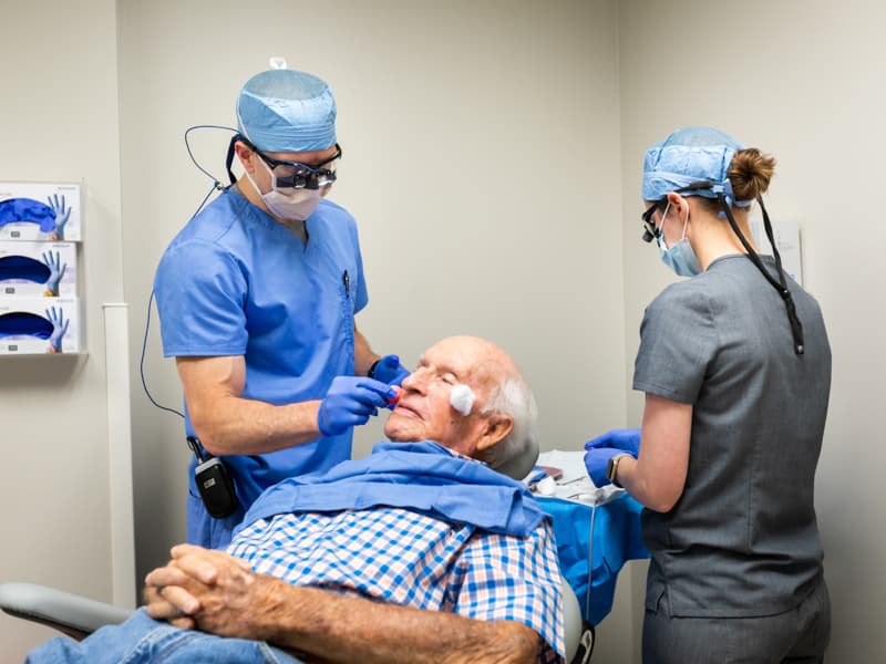 Dr. William Black, left, UMMC associate professor of dermatology, prepares to remove two skin cancers from Joseph Martin with help from Dr. Ritika Bhandari, dermatology resident.