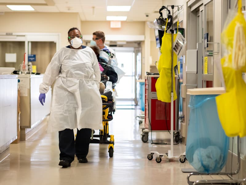 EMTs with American Medical Response wheel into the Adult Emergency Department an area nursing home patient having complications in his recovery from COVID.