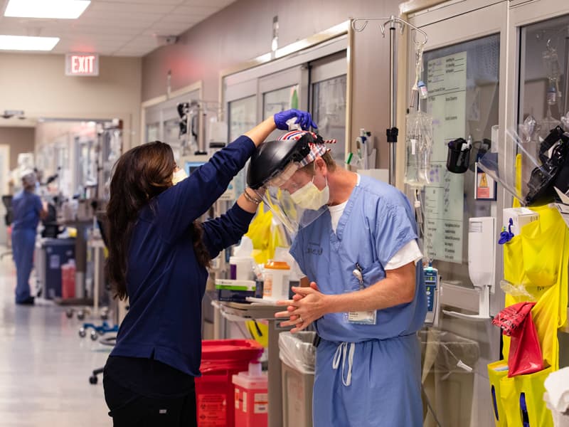 Ashley Moore, nurse manager on the medical ICU, helps Dr. Andy Wilhelm remove his facial shield following Wilhelm’s visit to the room of a COVID patient.