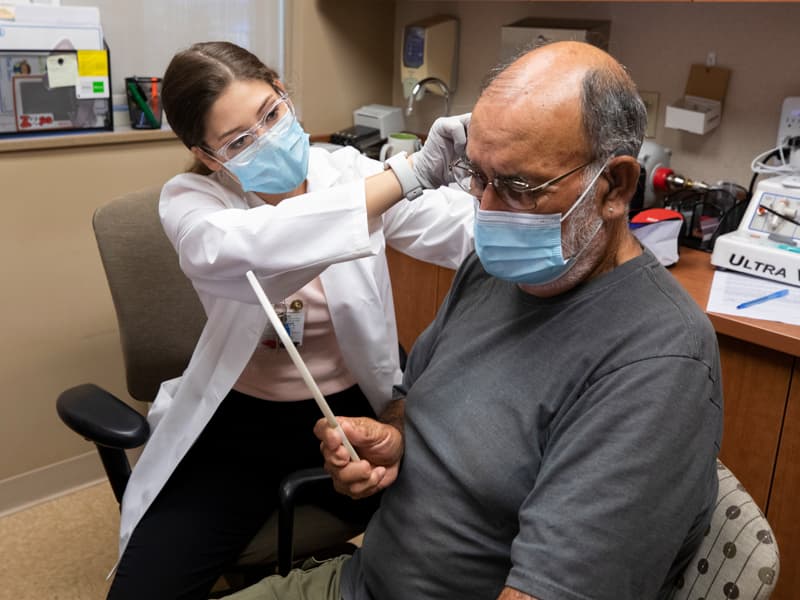 Doctor fitting man for hearing aid while man looks in mirror.