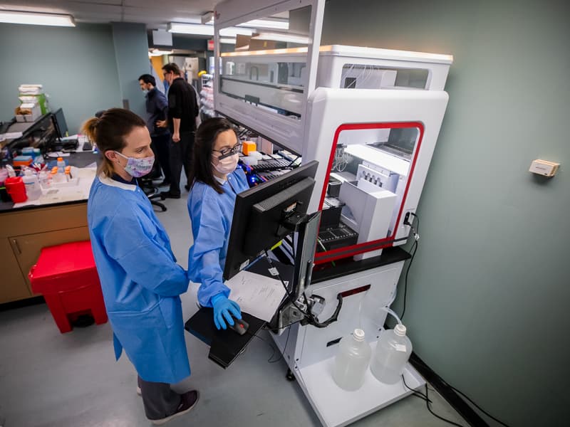 Registered medical technologists Jackie Starrett, left, and Sara Kemp watch the progress of COVID-19 samples on the new Biomek i7 robot in the molecular pathology laboratory.