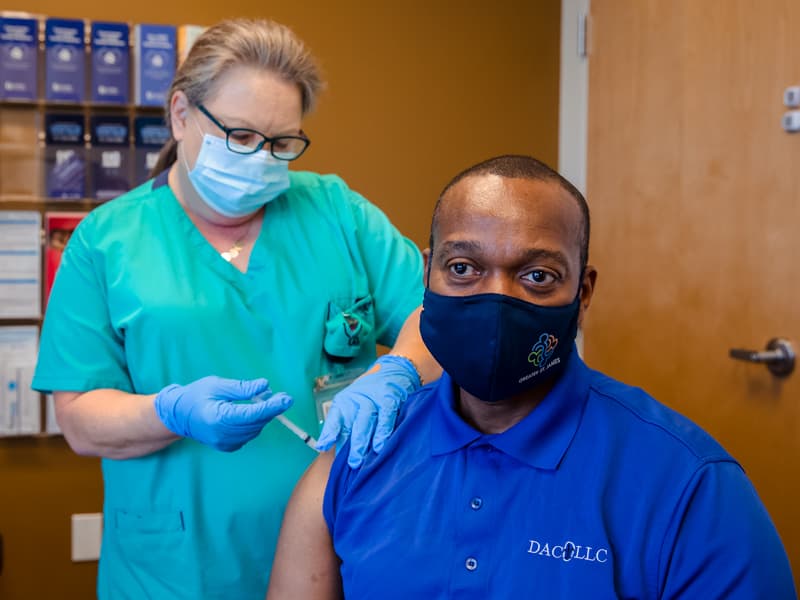 Babette Burke delivers the first dose of the Moderna COVID-19 vaccine to the Rev. Tony Montgomery.