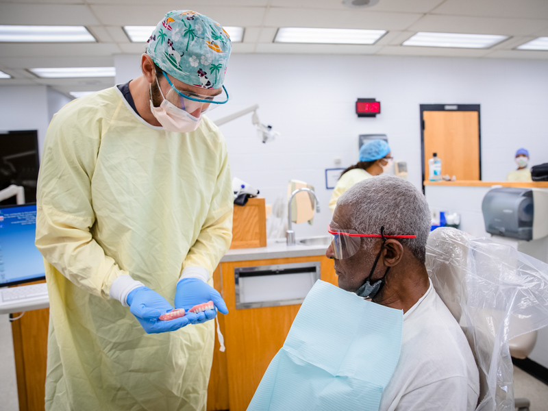 Patient Wilbert McGee gets a first look at his new dentures produced in a School of Dentistry laboratory by fourth-year student Trent Johnson, left.