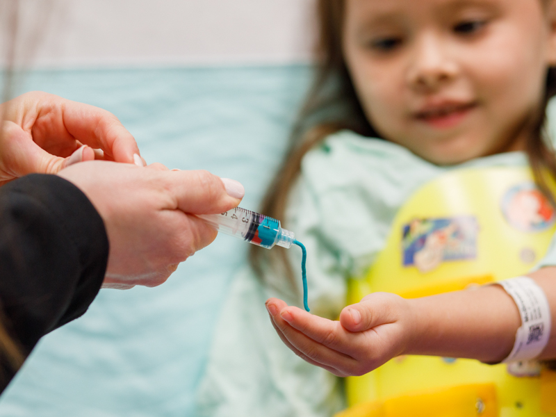 Elena watches at Play-Doh noodles come out of a syringe. Medical play such as this can ease children's fears.