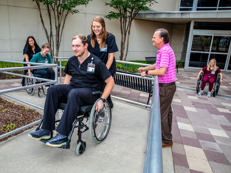 While Dr. Peter Giroux, right, observes occupational therapy students, from left, Hannah Heustress, Baylee Bryant, Dalton Frederick and Abbie Scott, practice wheelchair mobility by navigating a ramp outside the School of Health Related Professions building.