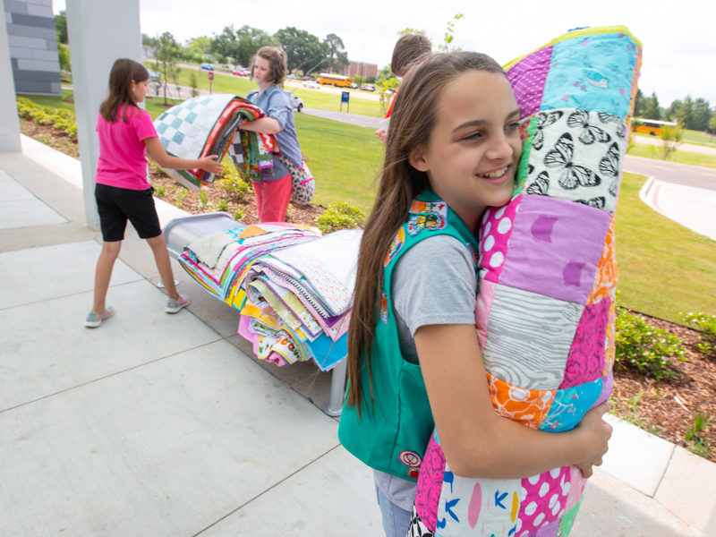 Junior Girl Scout Zoey Dowdy carries a stack of handmade quilts to present to the neonatal intensive care floors at the Kathy and Joe Sanderson Tower at Children's of Mississippi. Babies in the NICU will receive the future heirlooms.