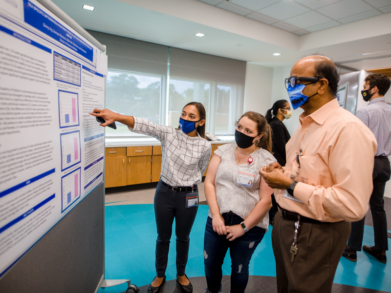Simmy Vig, left, a rising M2, points out details of her research to Addie Hitt, a fellow medical student, and Dr. Pradeep Alur, Vig's PReCEP mentor.