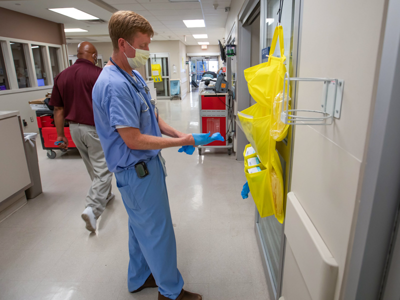 Wilhelm, division chief of Pulmonary and Critical Care Medicine, dons personal protective equipment before checking on a patient in the ED. 