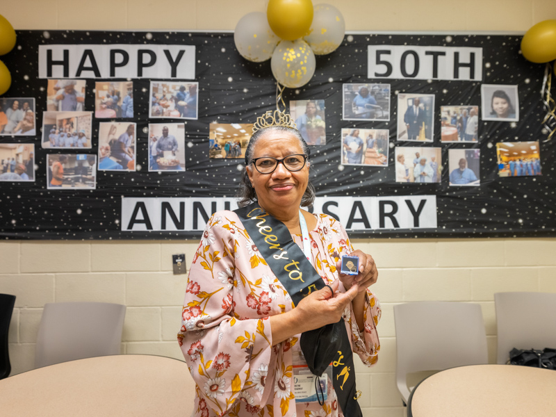 Verlyne Broadway holds up the pin she received in the room her co-workers decked out to honor her and her milestone anniversary.