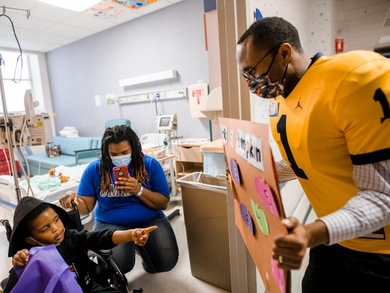 Hospital chaplain Mark Gilbert holds a Halloween game board for patient Cassidy Parker of Jackson as mom Natasha Parker takes a photo.