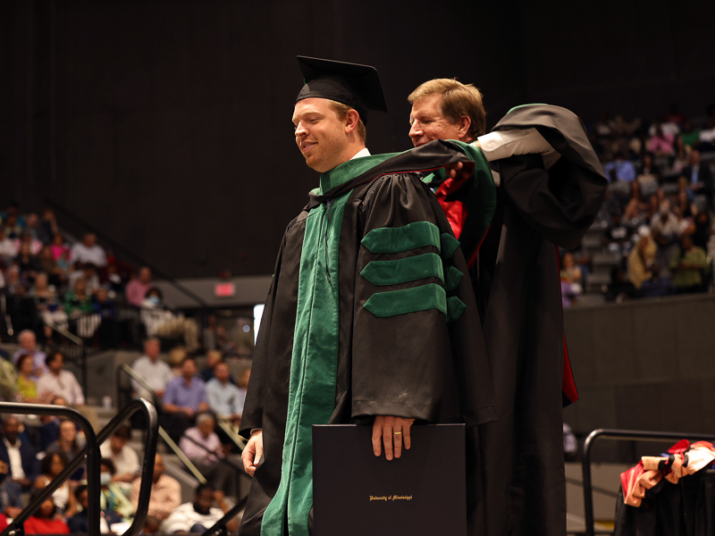 Dr. Mike McMullen hoods his son Ryan during UMMC commencement ceremonies. McMullen received a Doctor of Medicine degree.