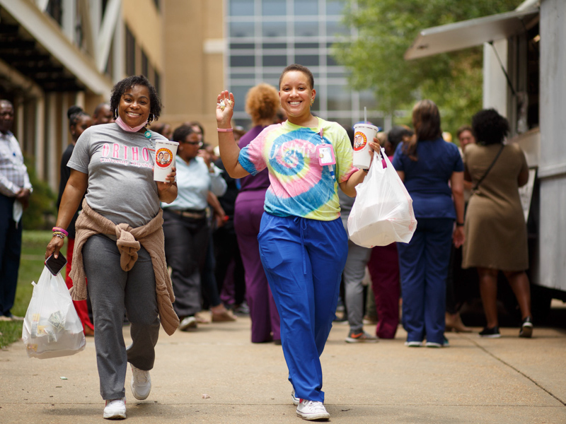 Customer care representative Tameyka Garner, left, and rehabilitation technician Princess Donelson head back to work Friday, loaded down with goodies from food trucks parked on the Guyton Building breezeway. Joe Ellis/ UMMC Communications