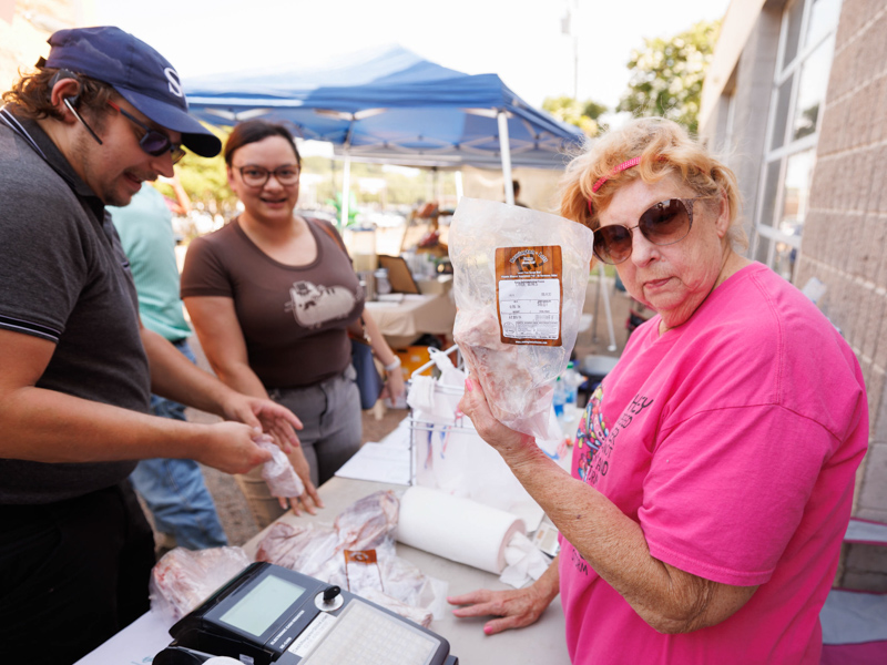 Carolyn Finchum, right, with Remington-Lott Farms in Canton, displays some of the farm's tasty merchandise as Dr. Amy Kohtz, an assistant professor in the Department of Psychiatry and Human Behavior and her fiancé Jason Lee buy tomahawk ribeye steaks and other items at Thursday afternoon's Farmer's Market behind Backyard Burger. The event was sponsored by the UMMC Office of Well-being. Joe Ellis/ UMMC Communications