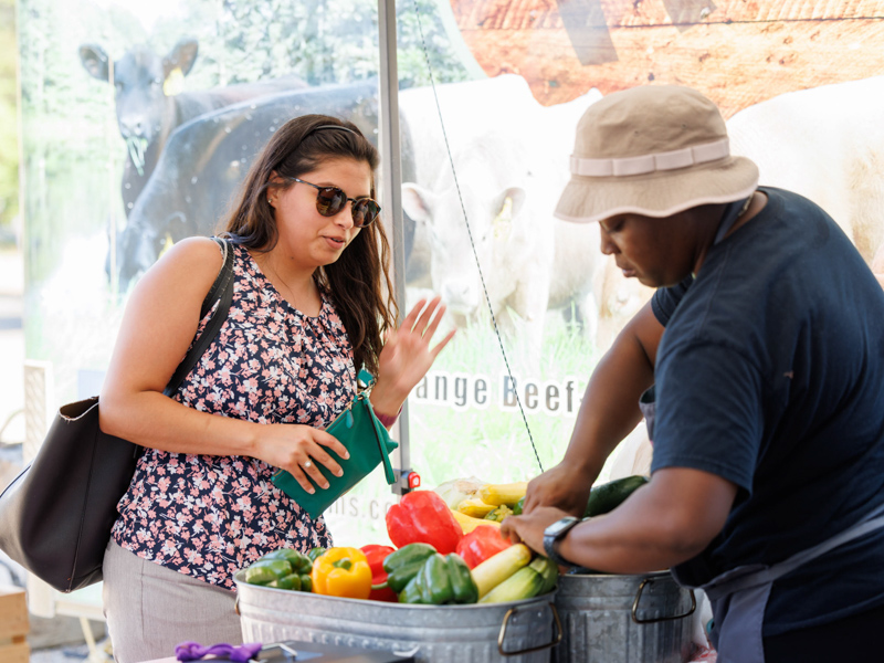 Aurora Diaz, a project manager with Neonatology, browses a selection of fresh vegetables with help from Michel'le Wheatley of Foot Print Farms at Thursday afternoon's Farmer's Market behind Backyard Burger. The event was sponsored by the UMMC Office of Well-being. Joe Ellis/ UMMC Communications