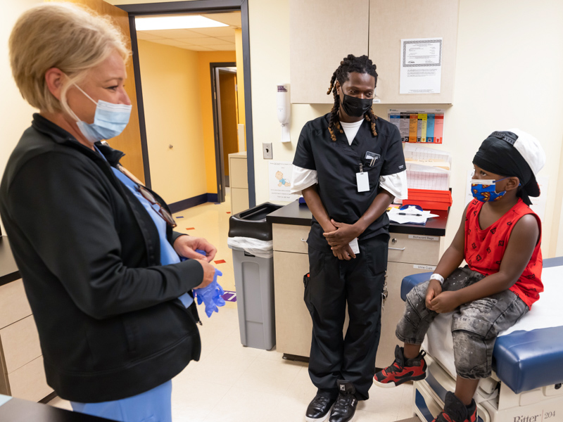 Nurse Kristi Chambley talks with Roderick Everett before giving him his COVID-19 vaccination as dad Roderick Smith looks on. Melanie Thortis/ UMMC Communications