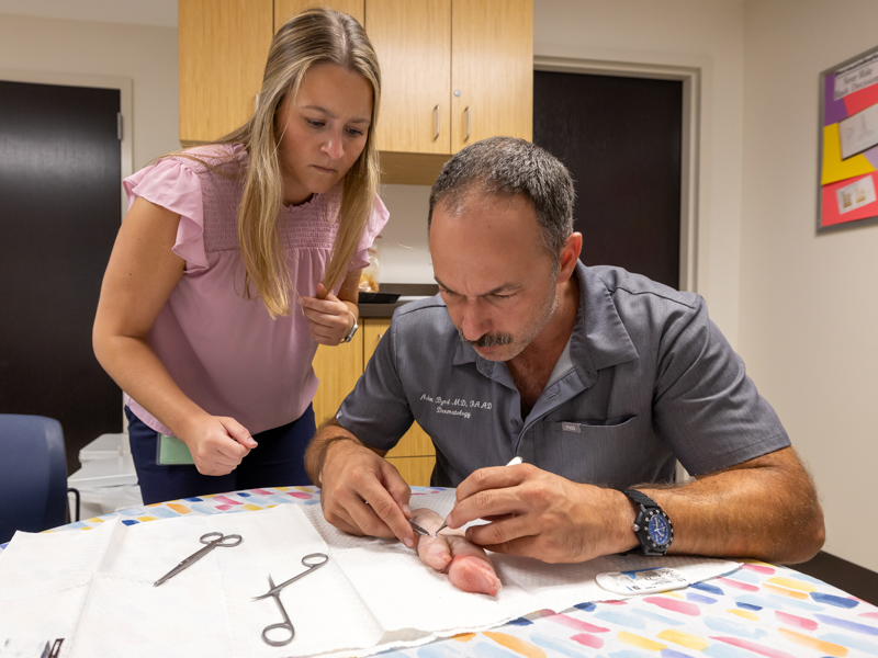 Using a pig's foot, Dr. Adam Byrd demonstrates for medical student Rachel Wilkinson the procedure for stitching up incisions. Jay Ferchaud/ UMMC Communications