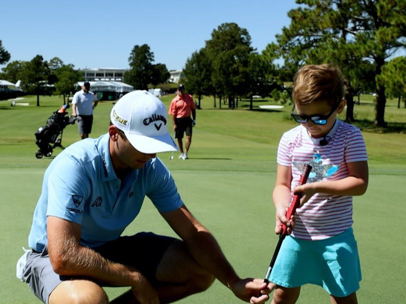 PGA golfer Sam Burns helps Mary Mosley line up her shot during a golf lesson.