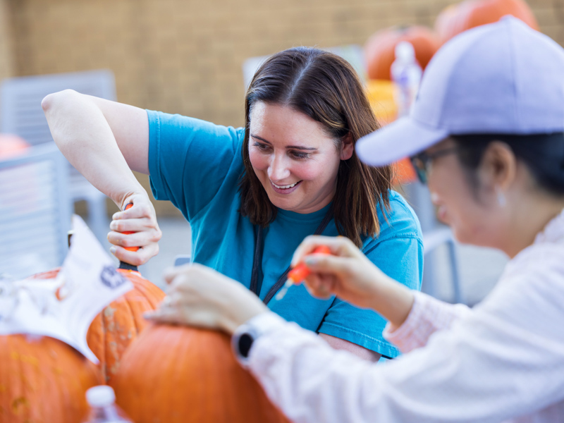 Dr. Jeannette Simino, associate professor with the Department of Data Science, carves pumpkins with students at the Translational Research Center. Melanie Thortis/ UMMC Communications 