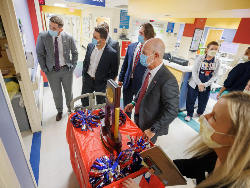 Ole Miss baseball players including, from left, Tim Elko, Dylan DeLucia and Hunter Elliott, plus coach Mike Bianco share their 2022 College World Series trophy with Children's of Mississippi patients during a visit Thursday. Joe Ellis/ UMMC Communications