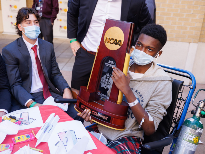 Children's of Mississippi patient Kamarion Jenkins of Tchula holds Ole Miss' 2022 College World Series trophy.