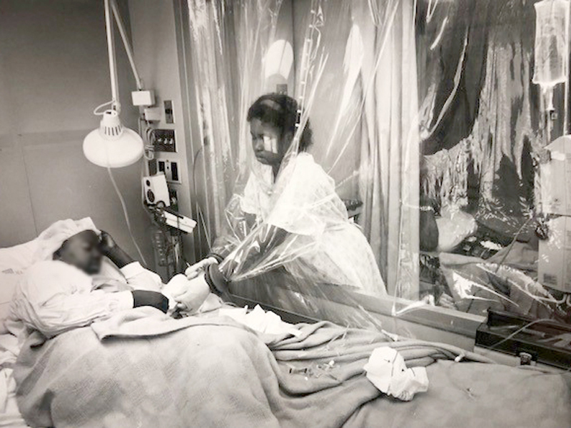 In this 1994 photo, a Medical Center nurse tends to a BMT patient by sticking her arms through a protective plastic curtain.
