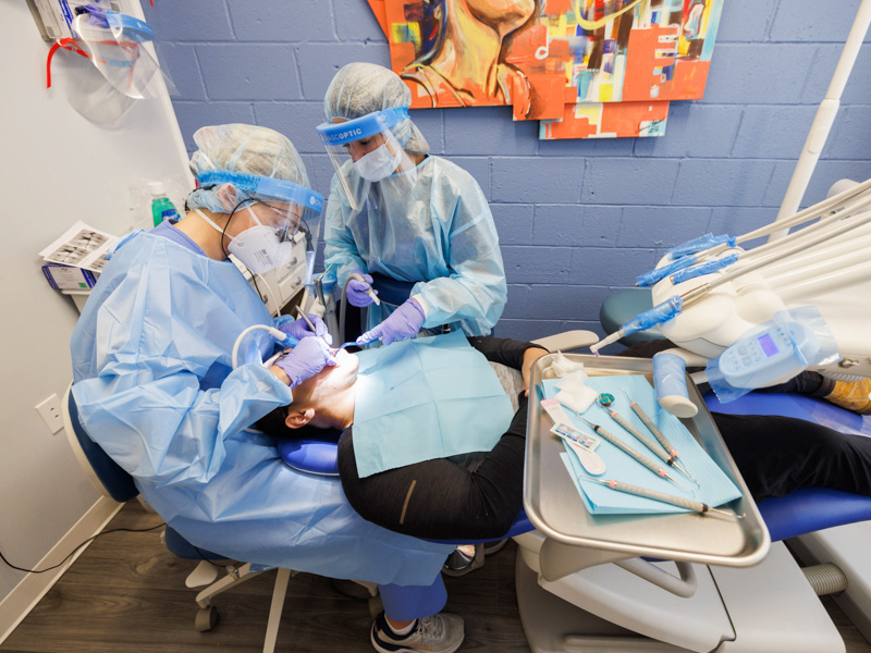 Senior dental hygiene student Mary Breland Cross, left, treats patient Zhenguo Xu at the Jackson Free Clinic as junior Morgan Leach assists. Joe Ellis/ UMMC Communications