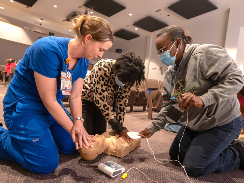 Nurse educator Martha Holmes coaches LaQuandra Jones and Myisha Jenkins in performing CPR and using an AED through Project ADAM. Melanie Thortis/ UMMC Communications