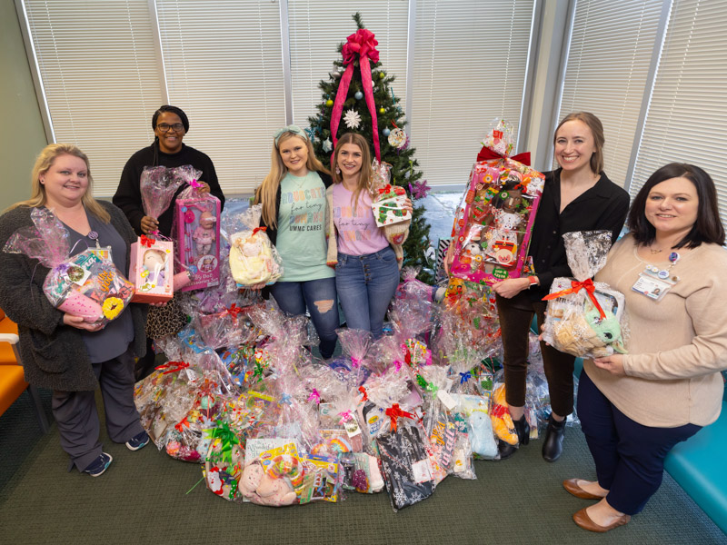 Smiling with a sampling of the 800-plus toys collected by UMMC CARES for the Children's Safe Center are, from left, Registered Nurse Care Coordinator Candise Walker, Project Manager Helean Hawkins, UMMC CARES President Emily Davis, UMMC CARES Vice President Katelyn Powell, Children's Safe Center director Courtney Helfrich, and nurse supervisor Amanda Sanford. Melanie Thortis/ UMMC Communications 